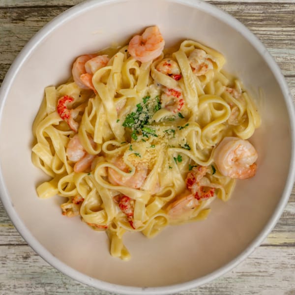 Creamy fettuccine pasta with shrimp, crawfish, parmesan cheese, and parsley in a white bowl.