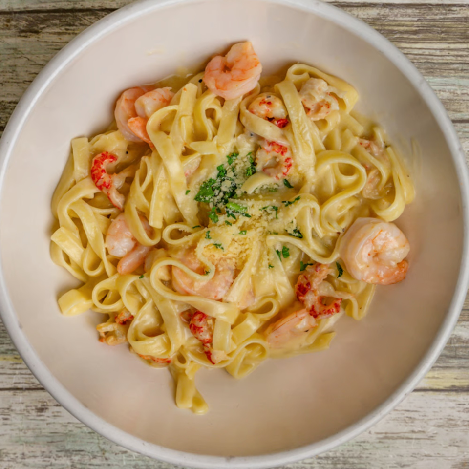 Creamy fettuccine pasta with shrimp, crawfish, parmesan cheese, and parsley in a white bowl.