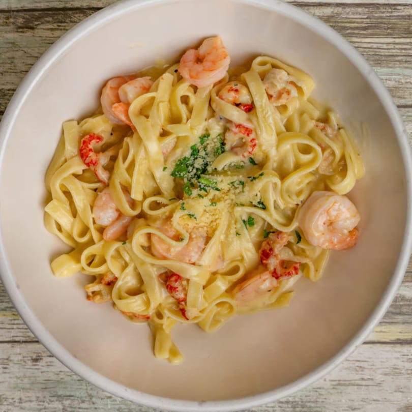 Creamy fettuccine pasta with shrimp, crawfish, parmesan cheese, and parsley in a white bowl.