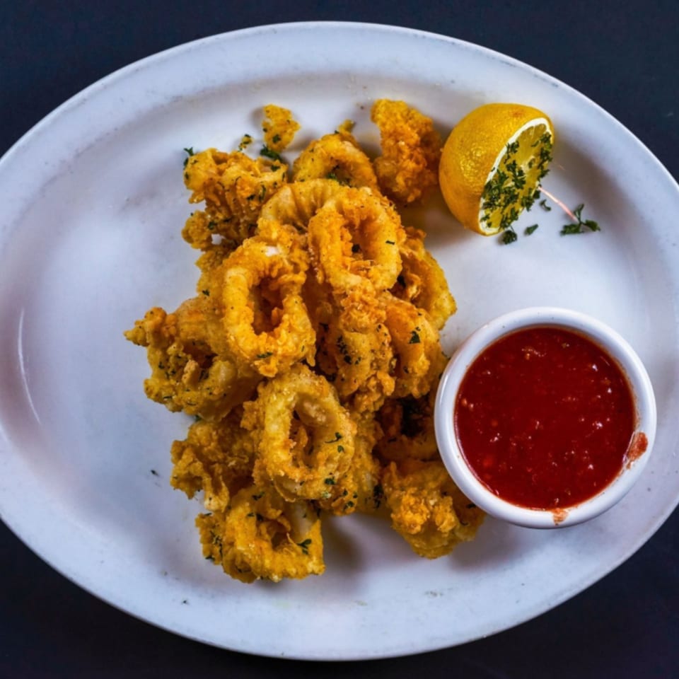 Golden fried calamari rings with a side of red marinara sauce and a lemon wedge.