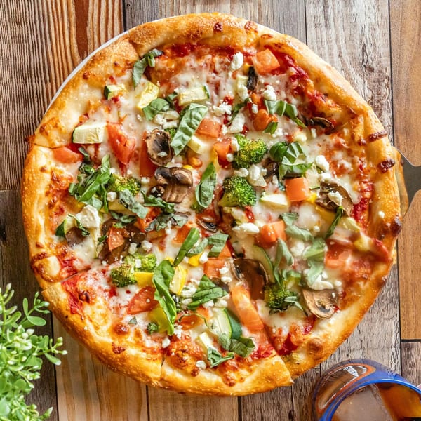 A vibrant vegetarian pizza with broccoli, mushrooms, tomatoes, zucchini, and feta cheese on a wooden table.