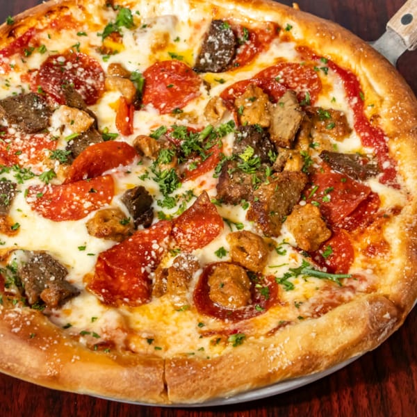 Close-up of a pizza with pepperoni, sausage, steak, and fresh parsley on a wooden table.