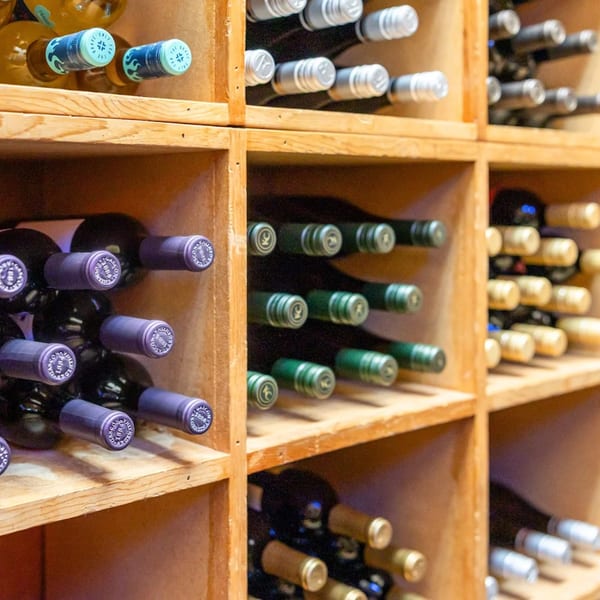 Wine bottles with various colored foil tops are neatly stored in wooden cubbies.