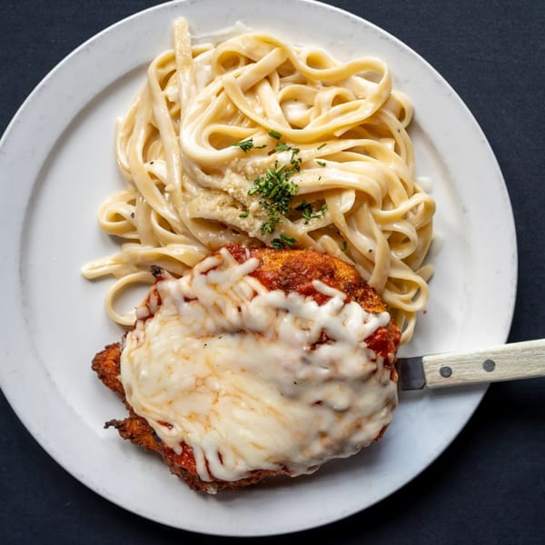 Chicken Parmesan with melted mozzarella, red sauce, and a side of fettuccine alfredo on a white plate.