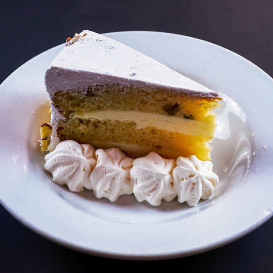 Slice of vanilla cake with white frosting and whipped cream dollops on a white plate.