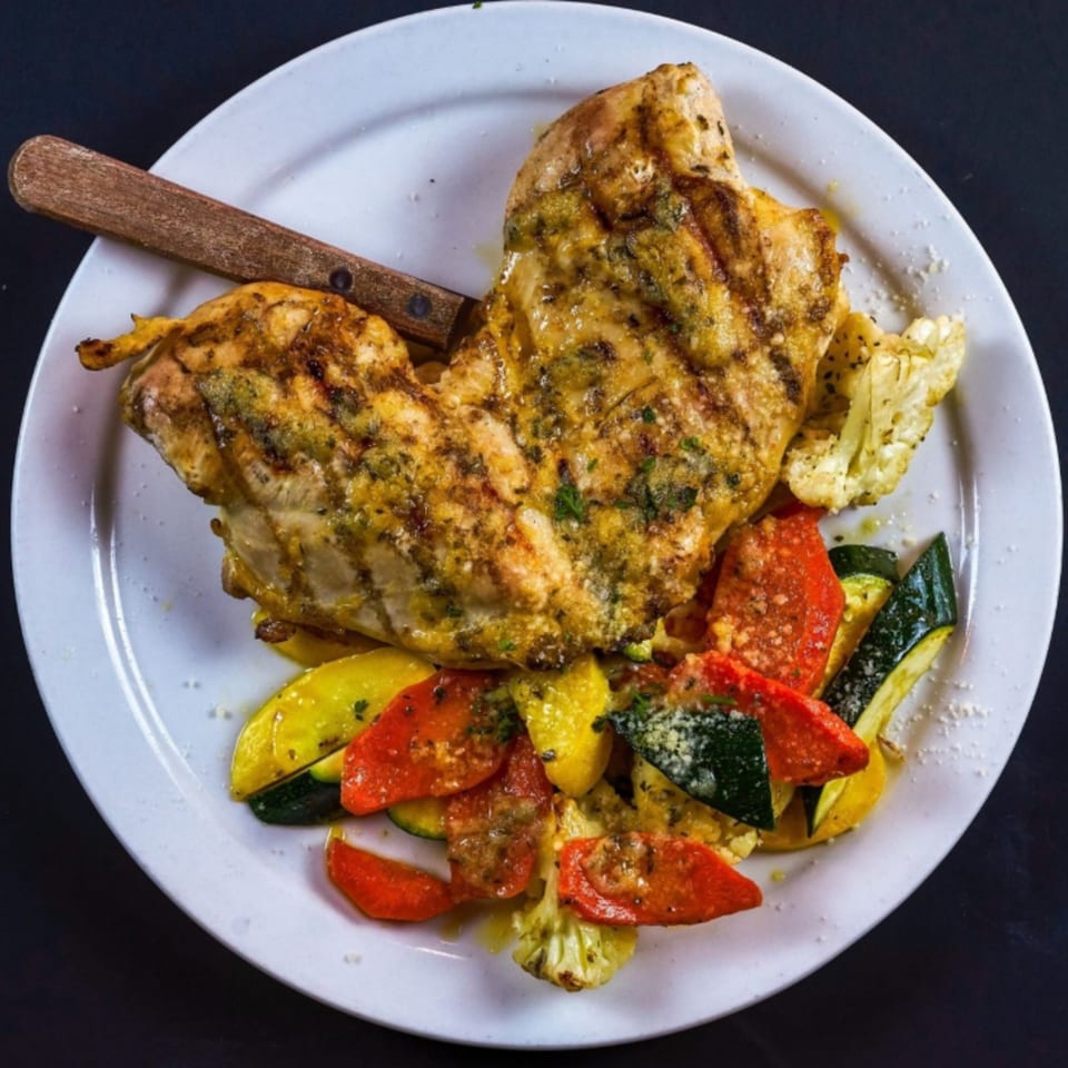 Grilled chicken breast with roasted zucchini, squash, red peppers, and cauliflower on a white plate.