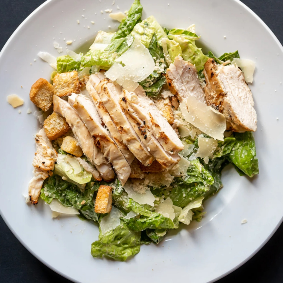 Grilled chicken Caesar salad with romaine lettuce, croutons, and parmesan cheese on a white plate.