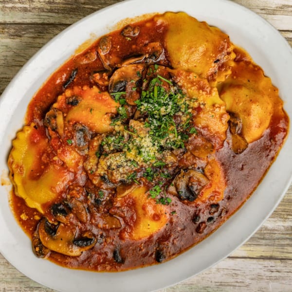 Ravioli with mushroom marinara sauce, topped with grated cheese and fresh parsley on a white plate.