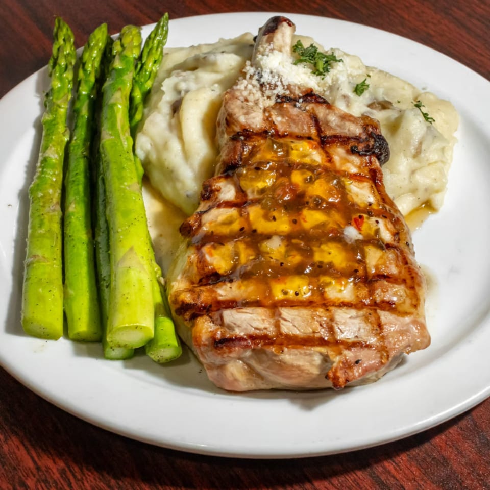 Grilled pork chop with a sweet glaze, mashed potatoes, and asparagus on a white plate.