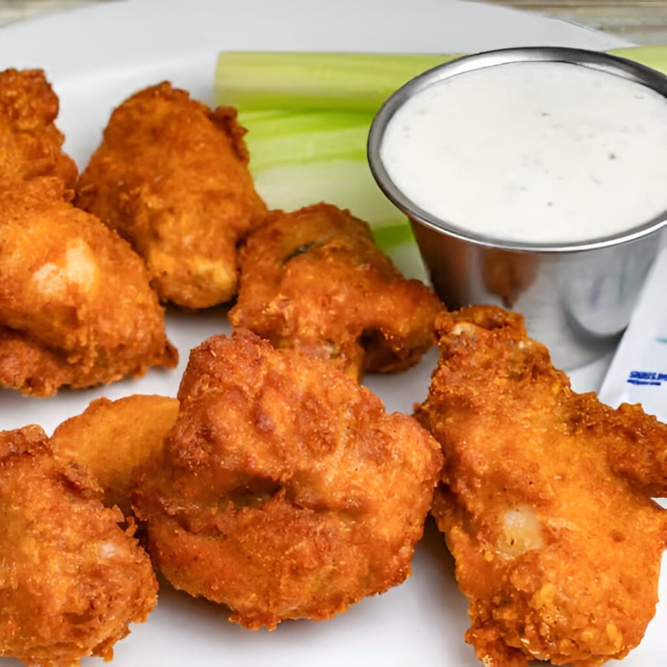 Crispy fried chicken wings with a side of celery sticks and ranch dressing on a white plate.